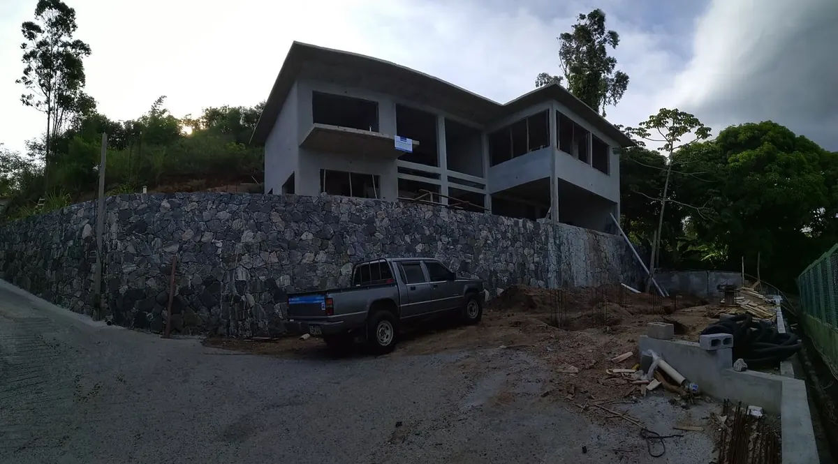 Residência em construção implantada em terreno de encosta, com muro de pedra junto ao acesso