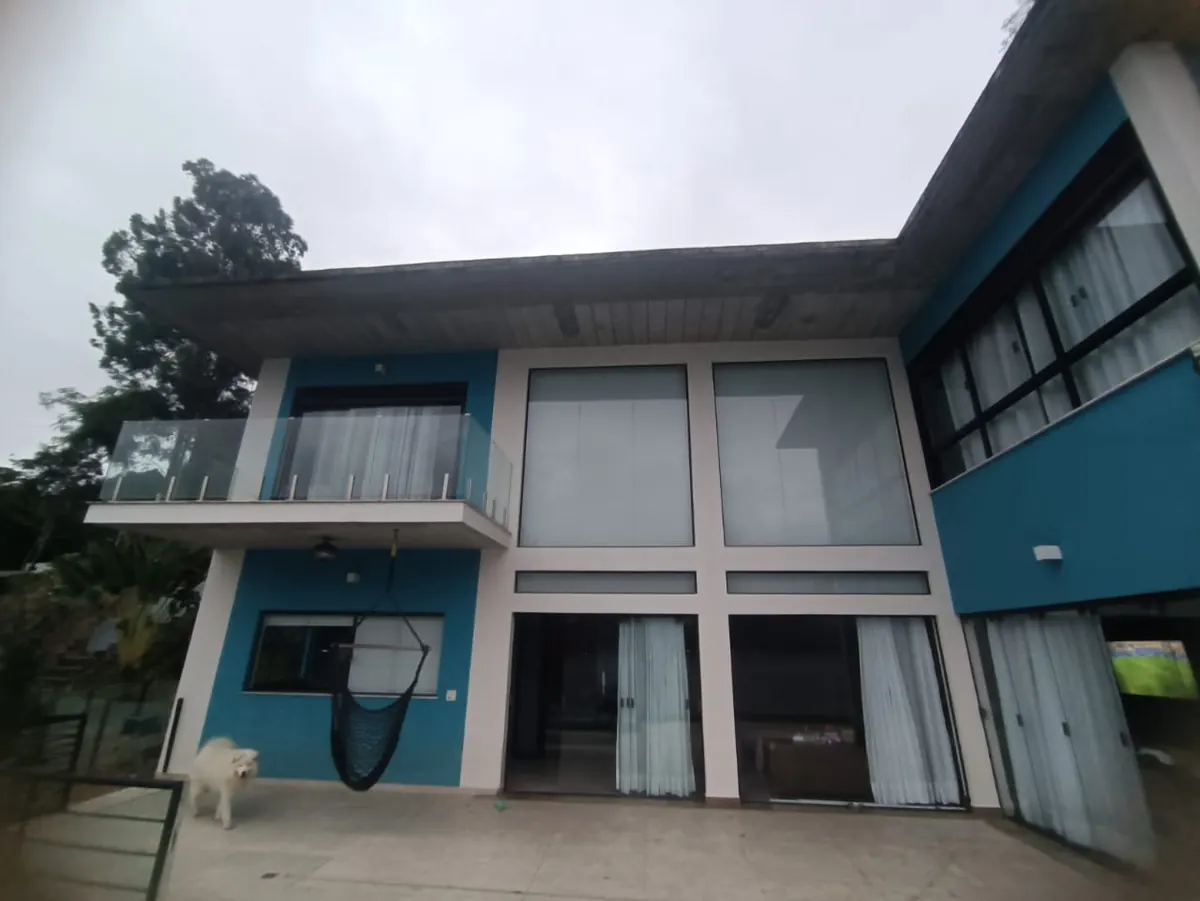Fachada concluída da residência, com esquadrias do piso ao teto e guarda-corpo de vidro