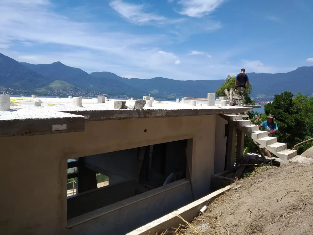 Equipe sobre laje concretada de residência em construção em São Sebastião, com o mar e a serra ao fundo