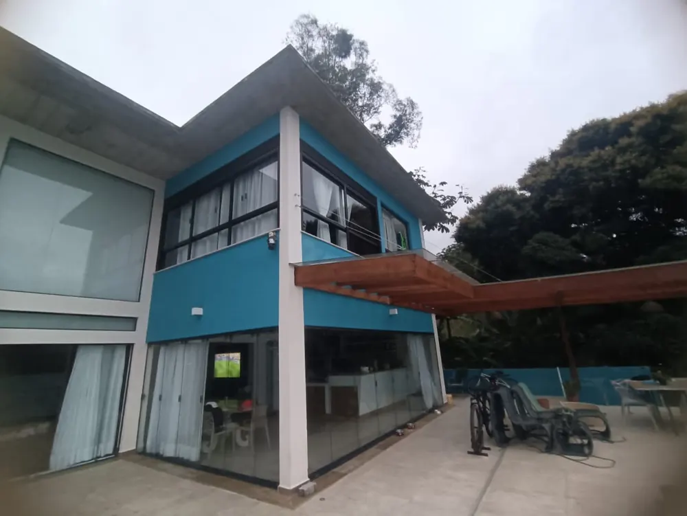 Residência concluída em São Sebastião, com fachada envidraçada, pergolado de madeira e terraço