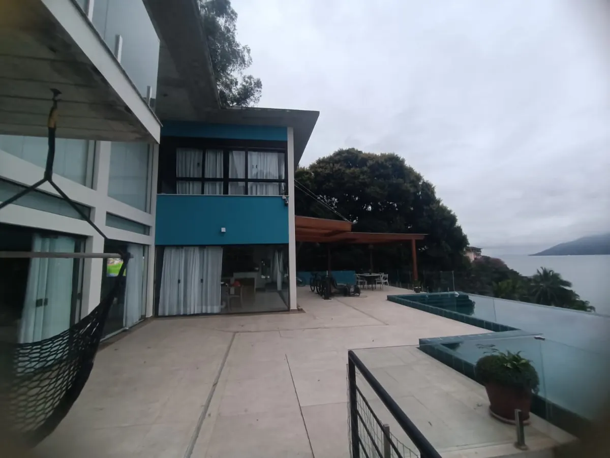 Terraço em porcelanato com pergolado e piscina de borda infinita voltada para o mar
